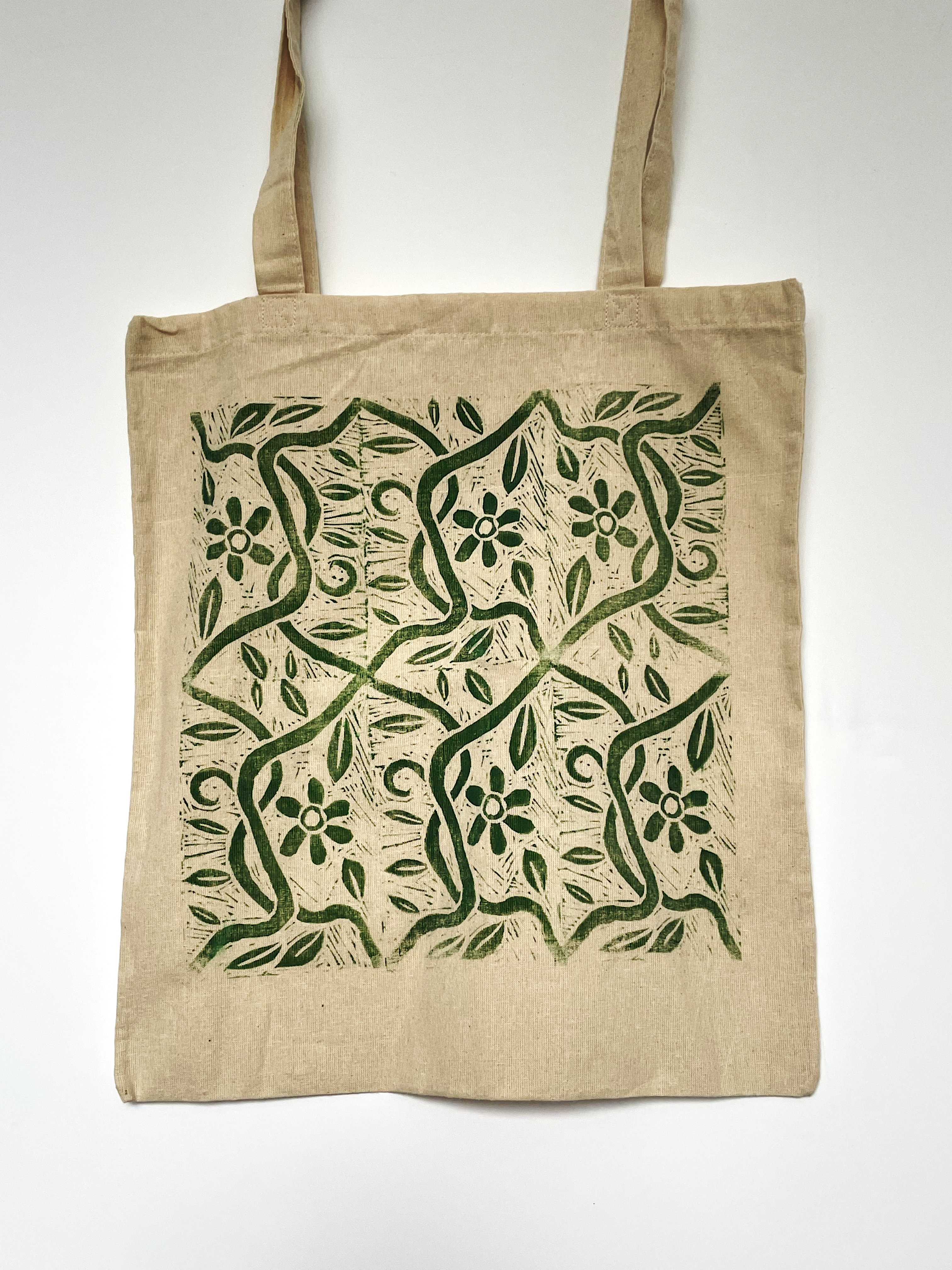 Off-white tote bag with a lino-printed repeating design of leaves and flowers in green